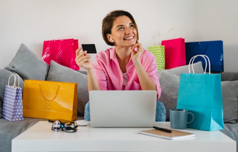 feliz-mujer-sonriente-camisa-rosa-sofa-casa-coloridas-bolsas-compra-tarjeta-credito-pagando-linea-computadora-portatil_285396-9240